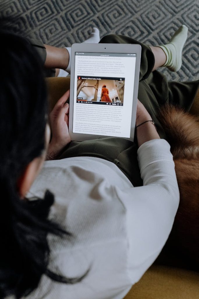 A woman reads an online article on a digital tablet while relaxing at home.